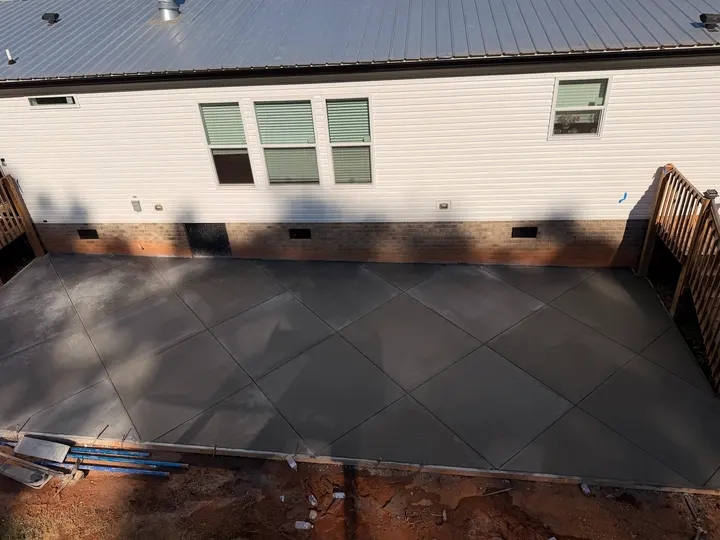 Wide concrete patio with diagonal joints beside a home, brick steps and an existing wooden deck.