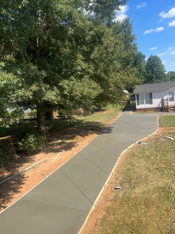 Fresh concrete driveway curving toward a home, with diagonal joints and forms along the edges.