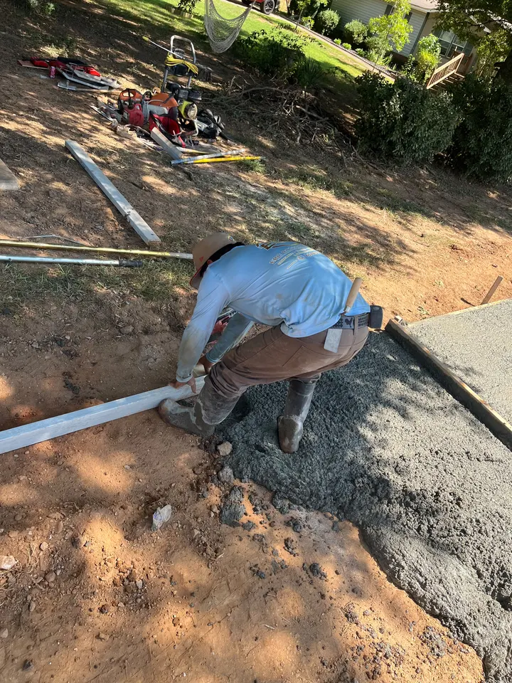 Worker drawing a long screed across fresh concrete during placement.