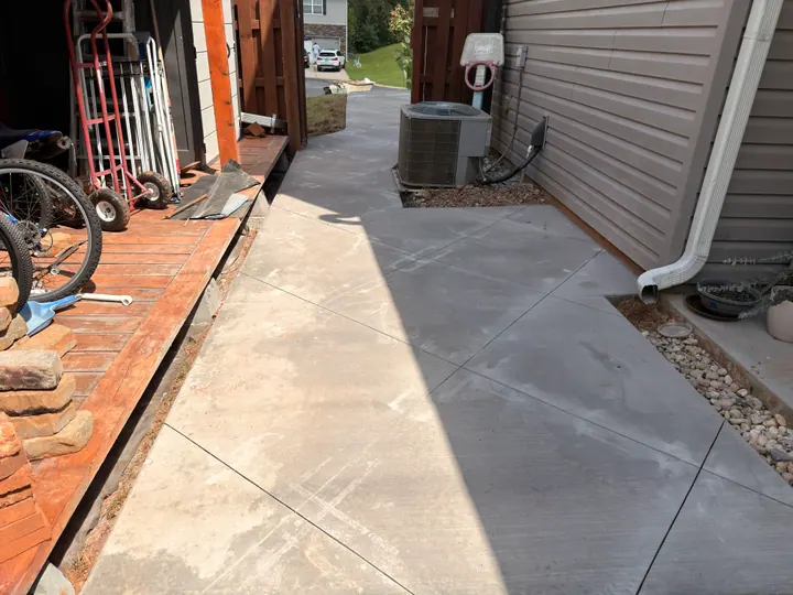 Concrete walkway between a brick porch and siding, with diagonal joints and a gravel border.