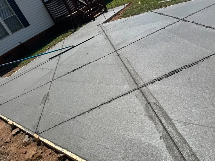 Close view of a textured concrete surface, joint pattern and formed edges beside a home.