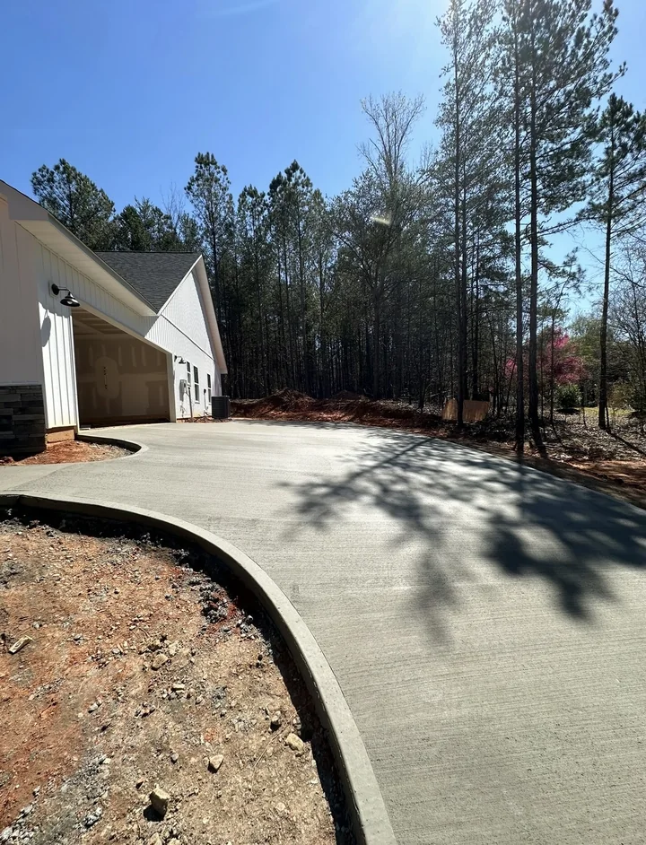 Curved concrete driveway leading to a home through a wooded lot